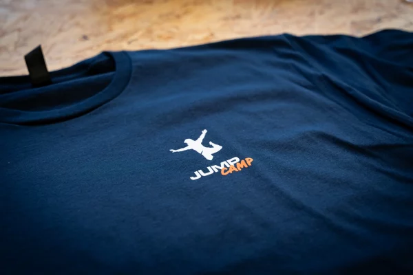 Detailaufnahme eines navyfarbenen Jump-Camp-T-Shirts mit weiß-orangefarbenem Brustlogo.